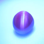 Alexandrite cat’s-eye cabochon showing reddish-orange tones under warm lighting.