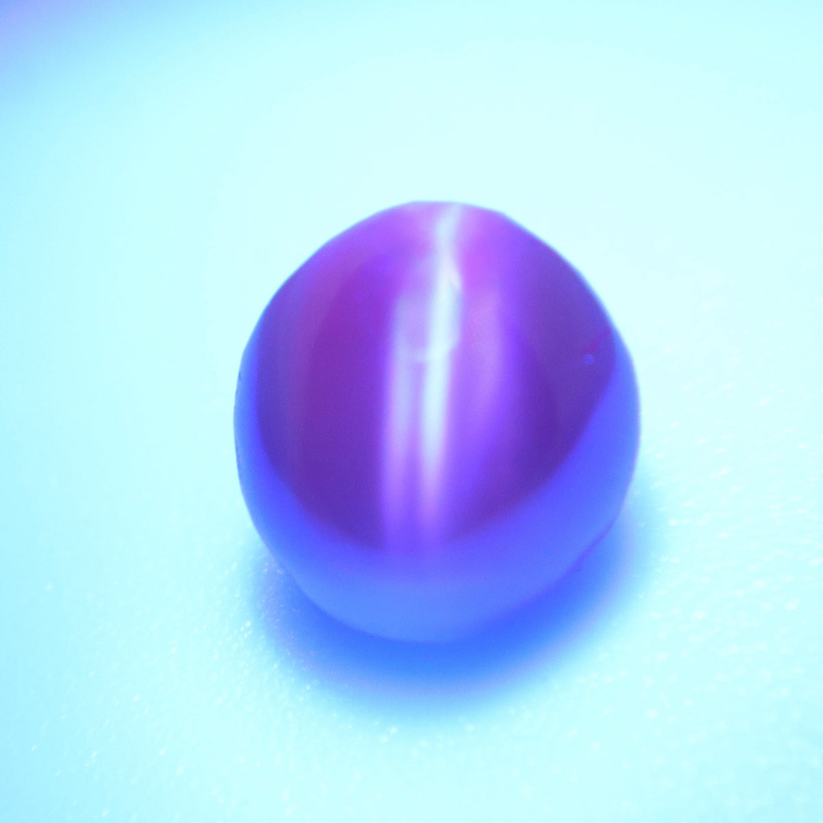Alexandrite cat’s-eye cabochon showing reddish-orange tones under warm lighting.