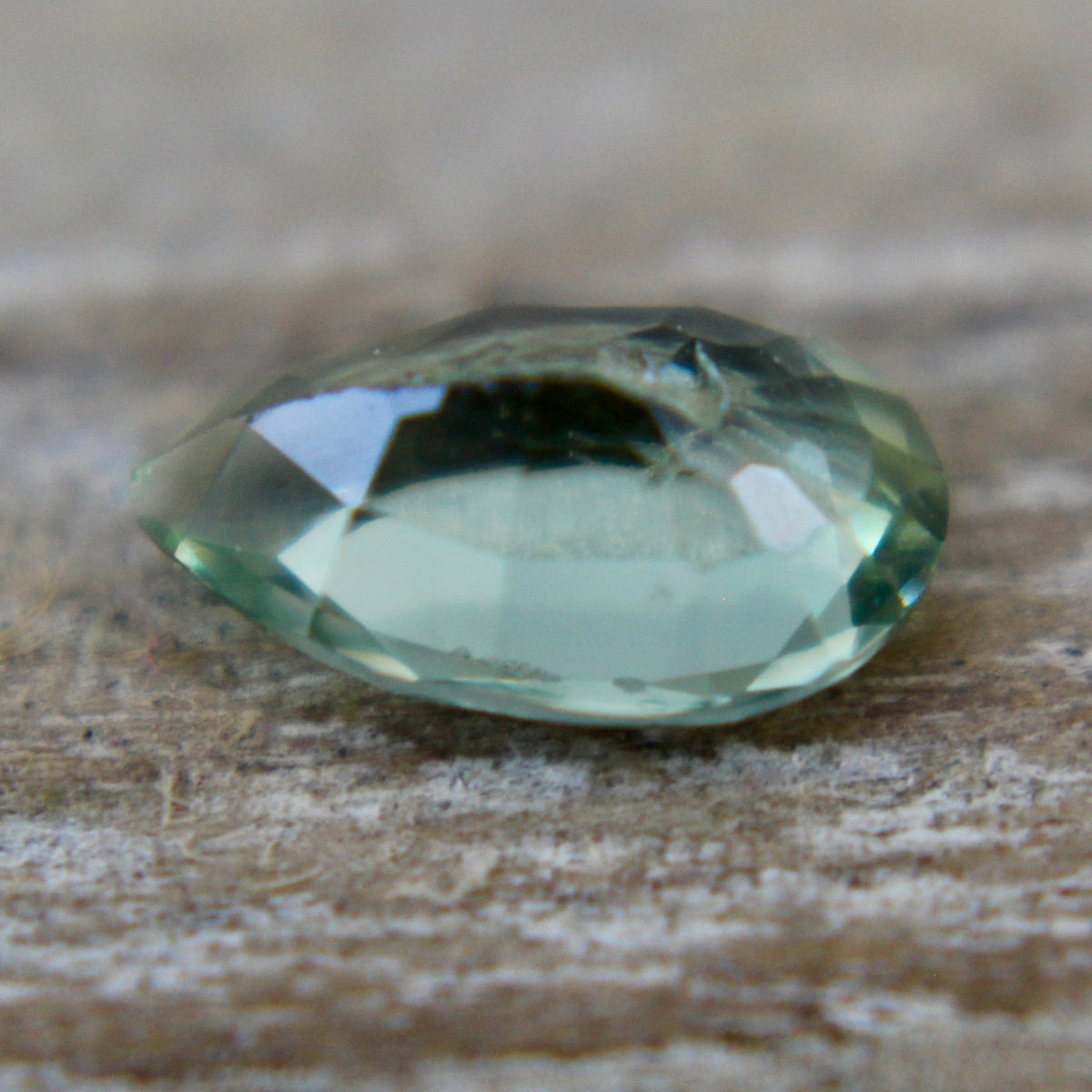 Angled view of a green pear-cut sapphire showing its crown facets and tapered point.