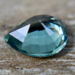 Angled view of a green pear sapphire showing its crown facets and tapered point.