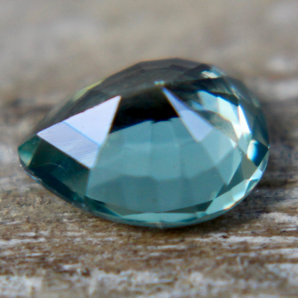 Angled view of a green pear sapphire showing its crown facets and tapered point.