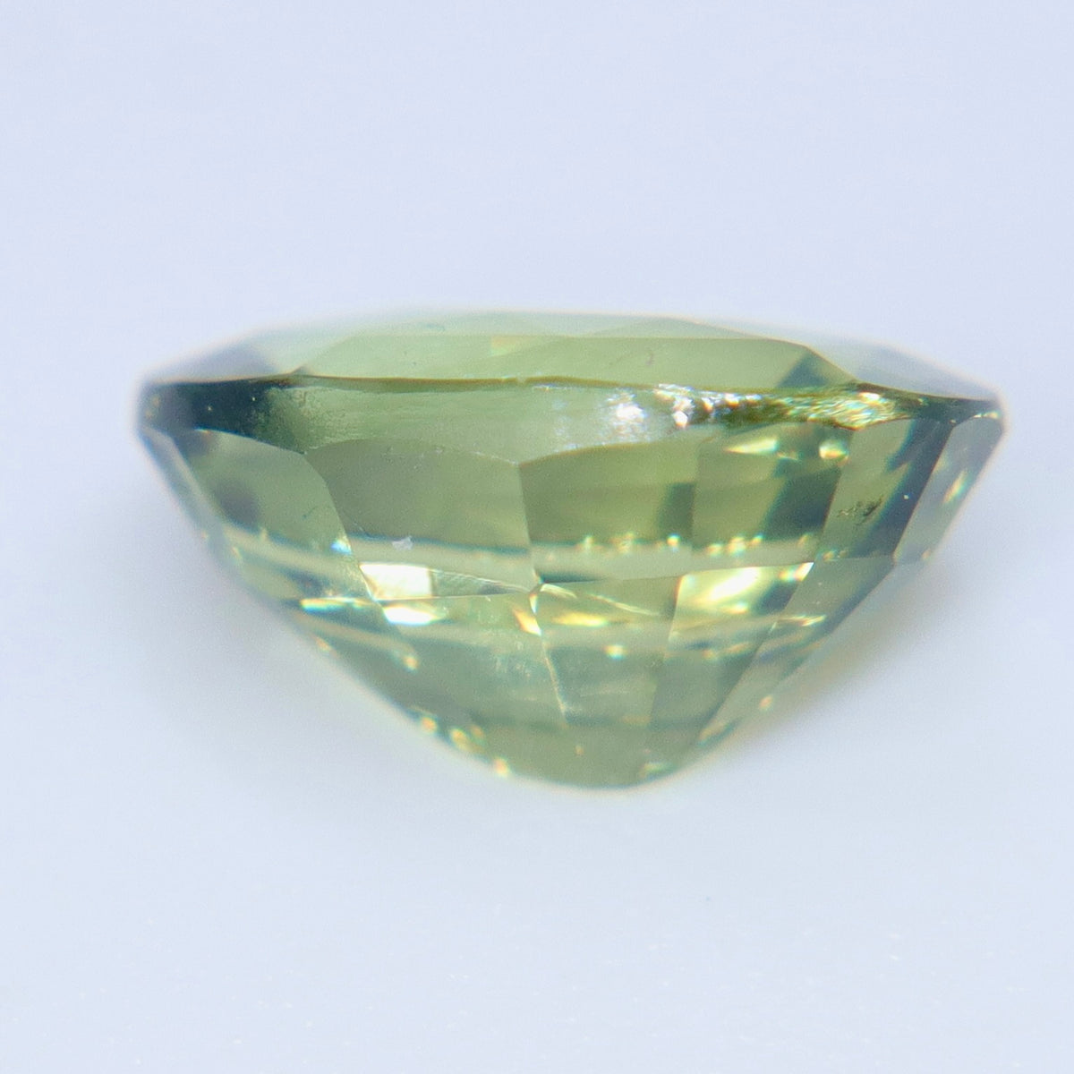 Angled view of a natural oval alexandrite showing pale green tones and crown facets.