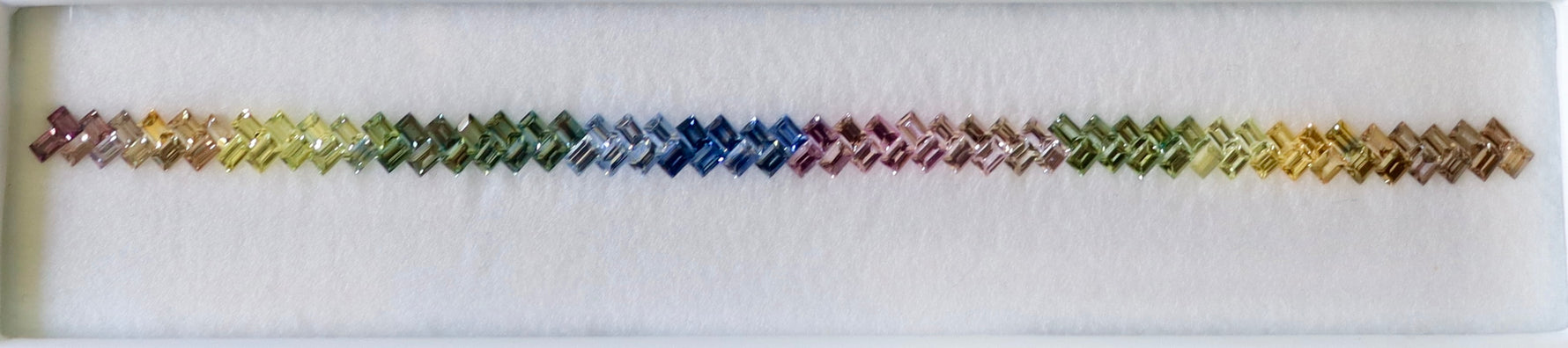 Close view of cut and polished sapphire stones arranged as a rainbow, earth sourced colored gemstones