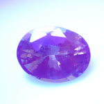 Oval alexandrite appearing violet-purple against a pale background.
