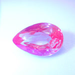 Pear-cut alexandrite appearing bright pink against a pale background.