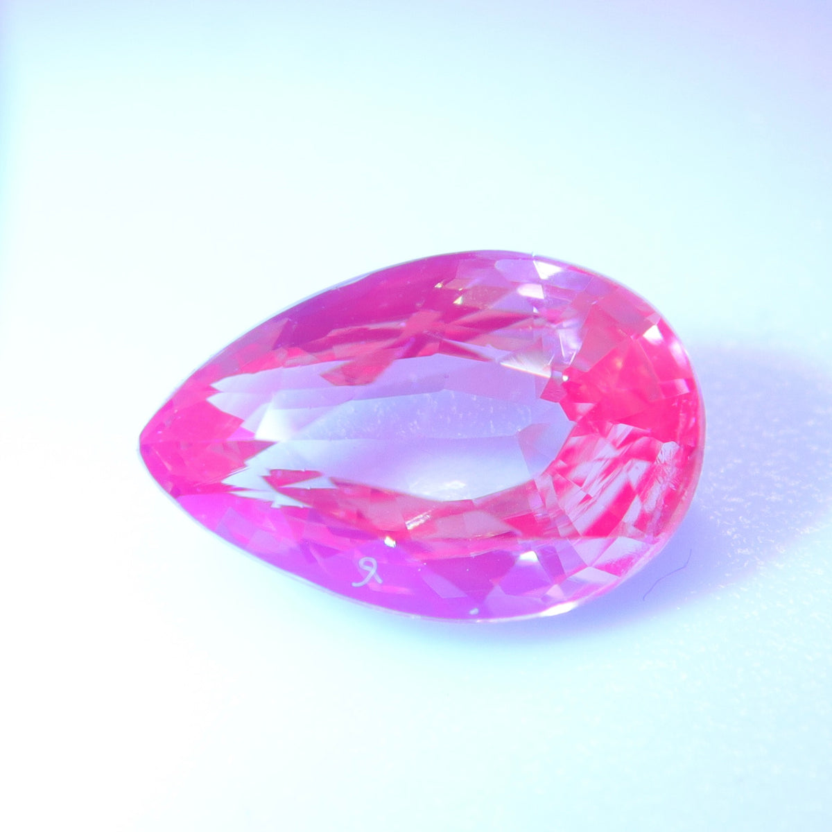 Pear-cut alexandrite appearing bright pink against a pale background.