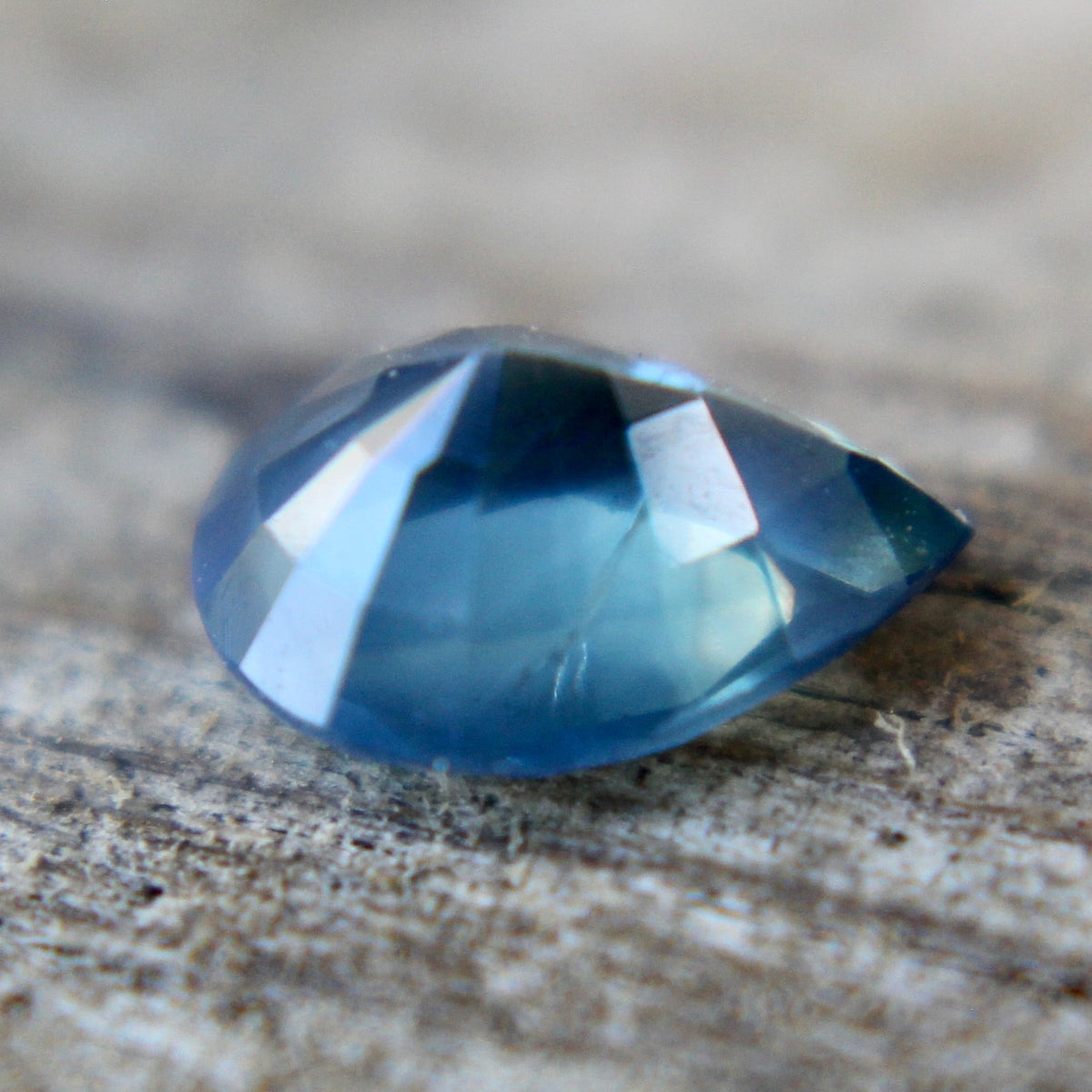 Angled view of a blue-green sapphire showing its pear shape and crown facets