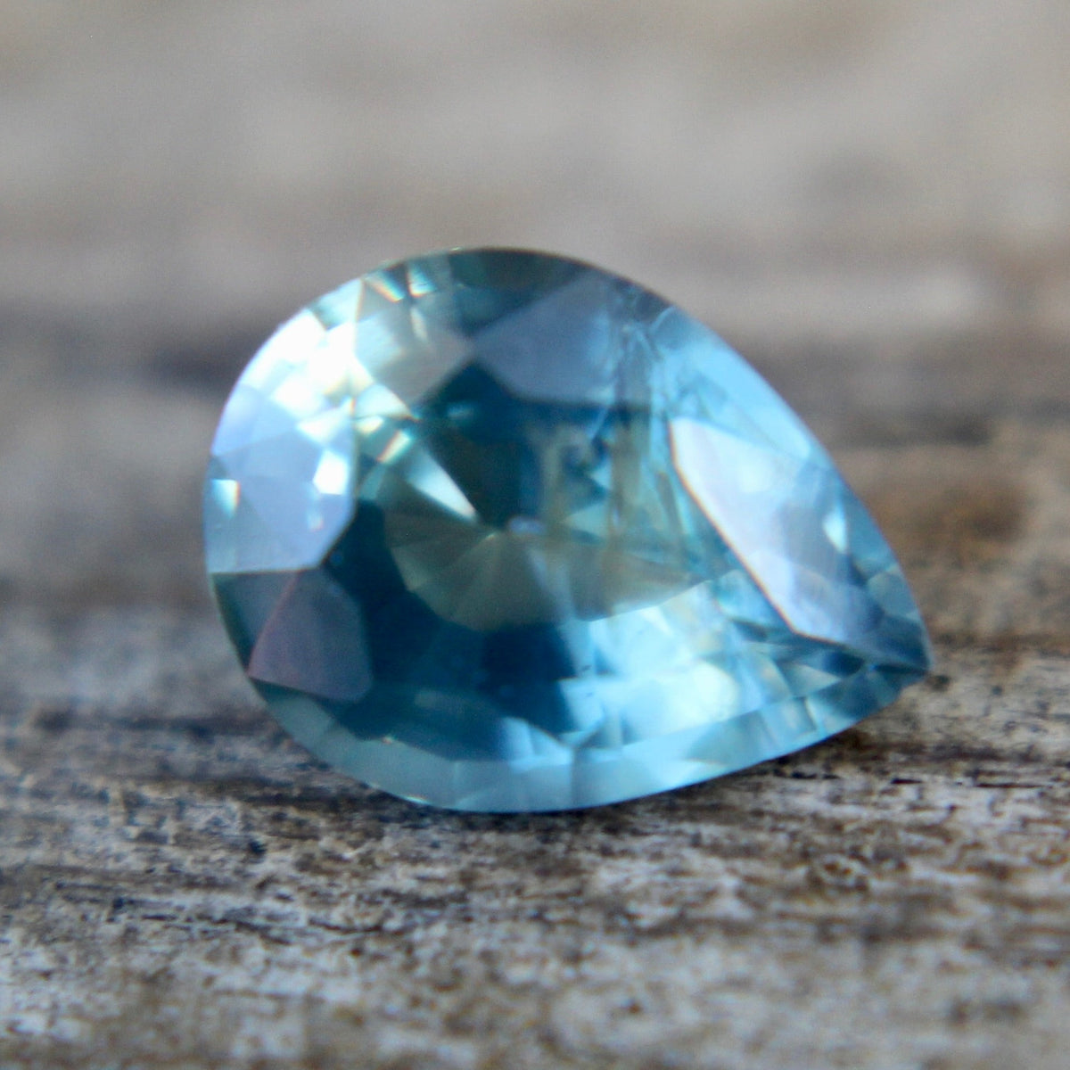 Underside view of a blue-green pear sapphire showing its pavilion facets and tapered point