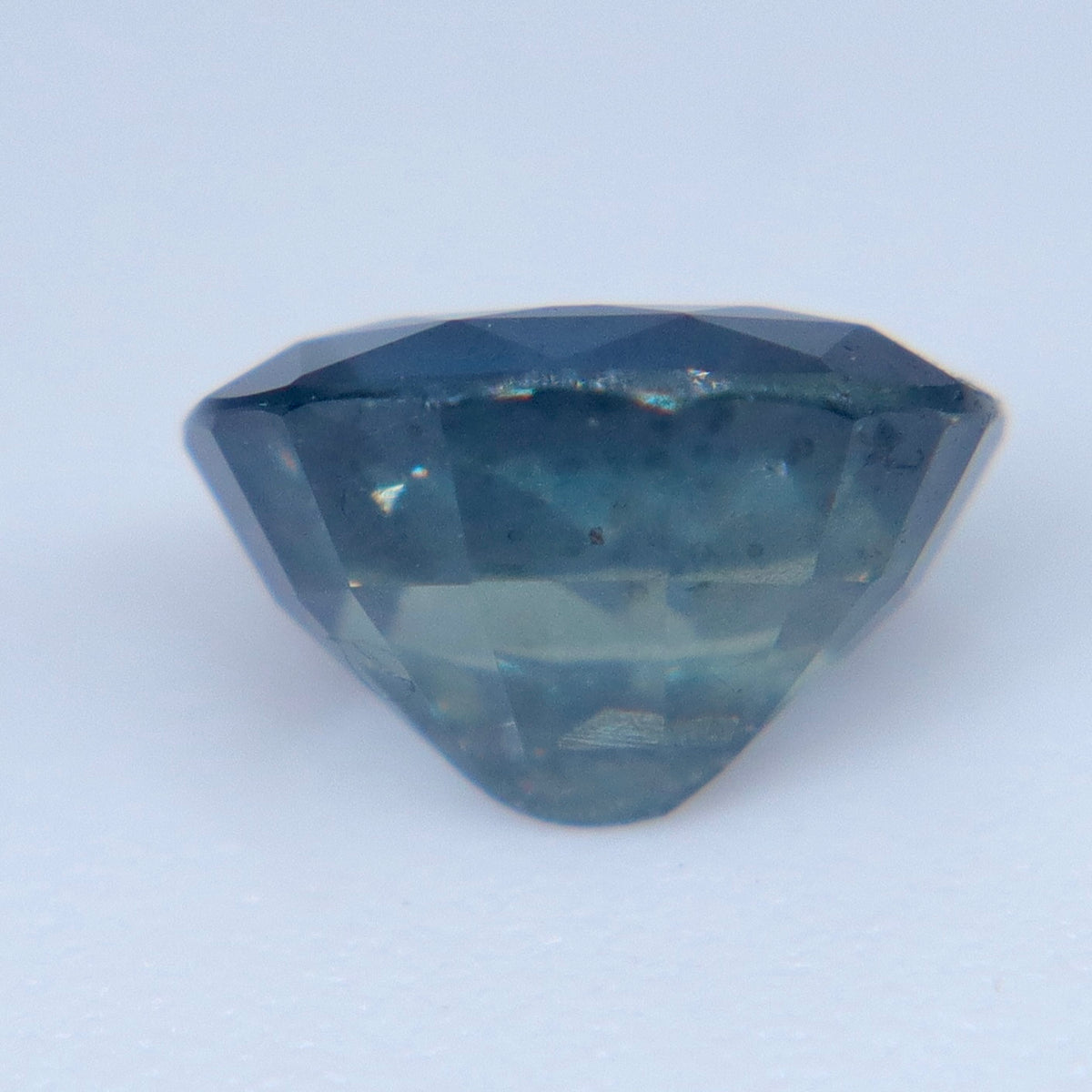 Face-up close-up of a faceted oval sapphire with bright reflections on a pale background