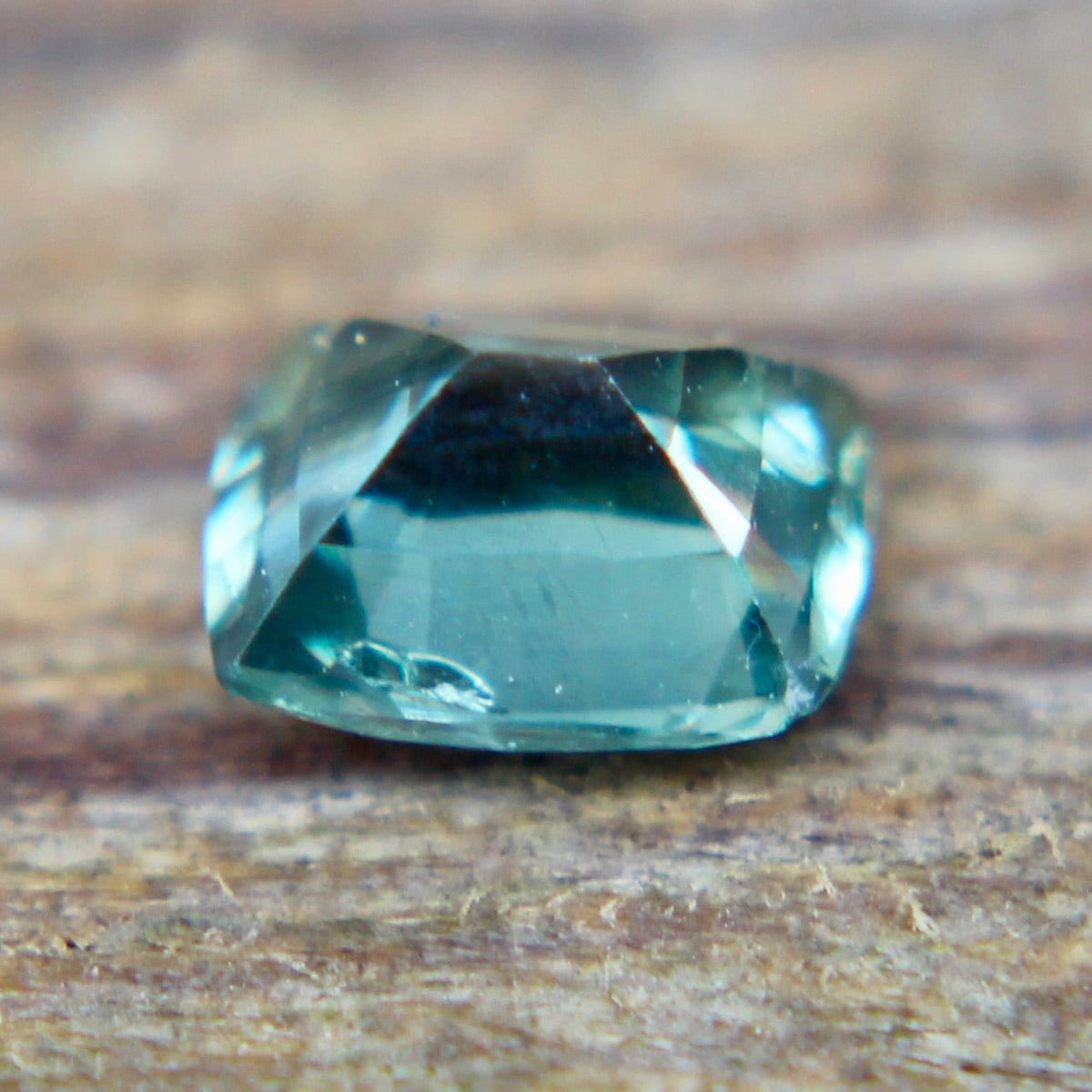 Angled view of a green cushion-cut sapphire showing its crown facets