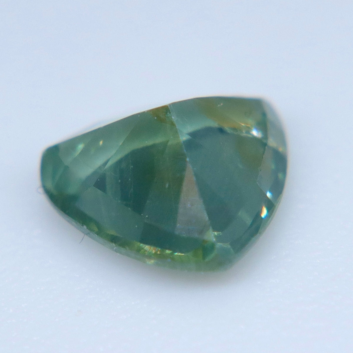 Angled view of a green Ceylon sapphire showing its rounded triangular outline and facets