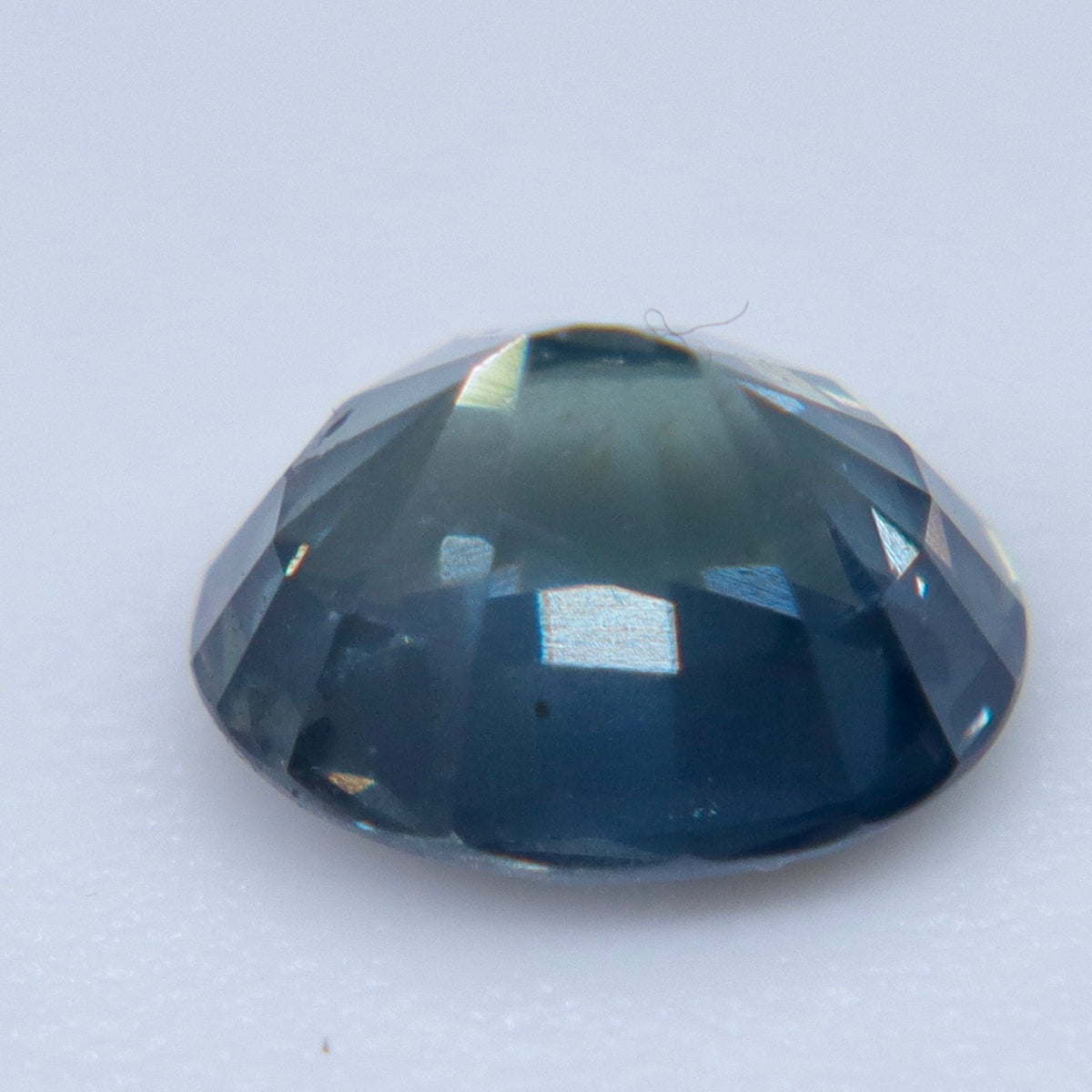 Angled close-up of a loose oval sapphire showing its crown and dark blue-gray tones