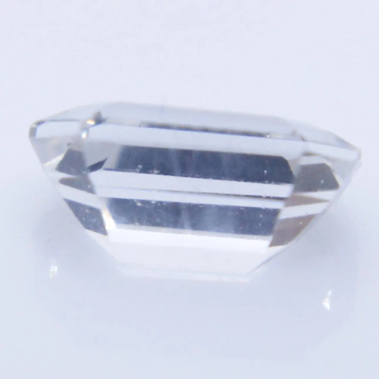 Close up of faceted white sapphire emerald cut showing clean brilliance and step-cut reflections
