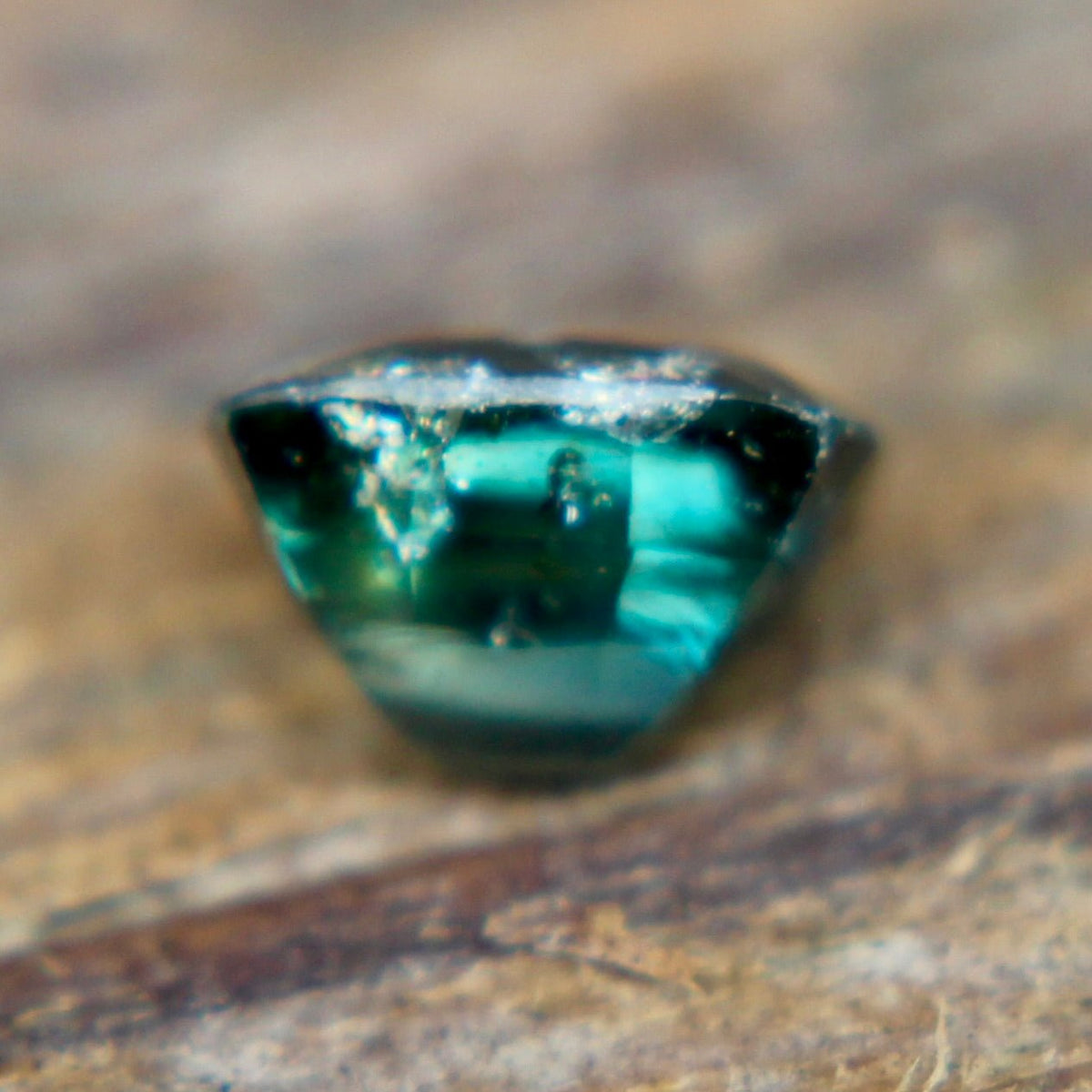 Angled view of a teal green cushion-cut sapphire showing its crown facets